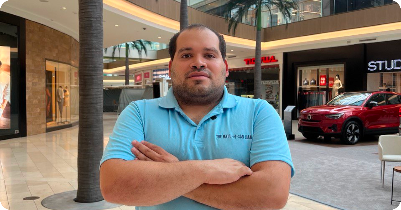 Hombre con camiseta de The Mall of San Juan con sus brazos cruzados, mirada fija y posando dentro del centro comercial.